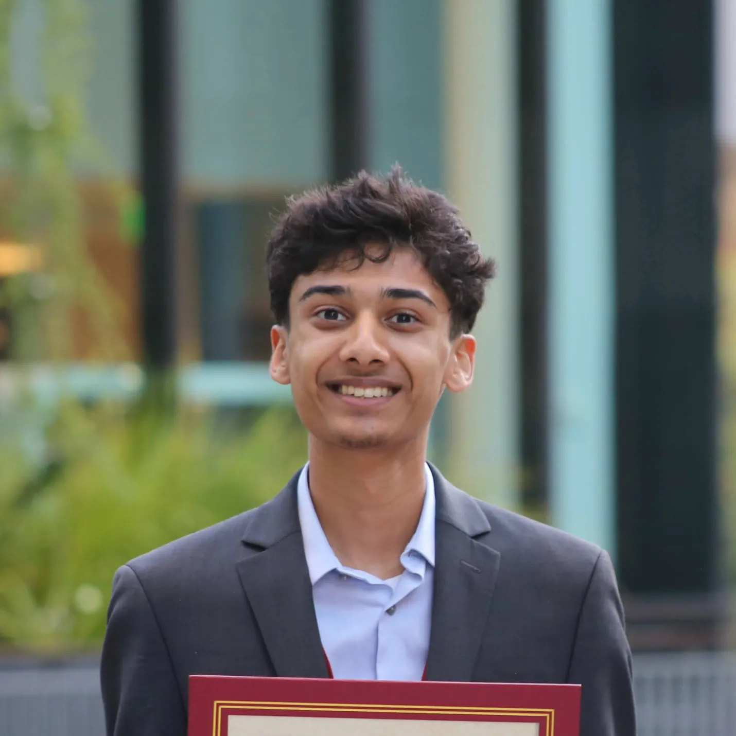 Veer smiling, holding a framed award